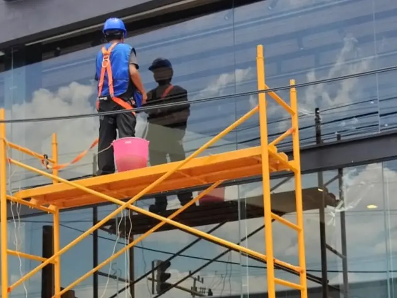 Colaborador de BioClean con casco y arnés limpiando cristales en altura desde un andamio en Puebla